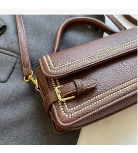 Close-up of brown litchi grain leather bag with gold buckle and decorative stitching