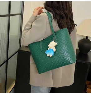 Detail of dark green tote bag with embossed letters and a cute plush bear pendant