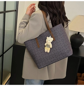 Detail of grey tote bag with letter prints and a cute bear charm on a model shoulder