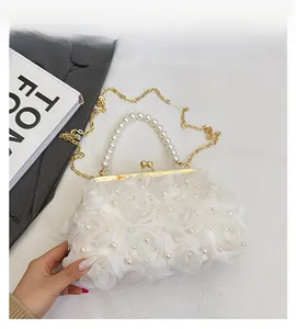 Détail d'une pochette blanche avec roses en tissu, perles et fermoir boule dorée