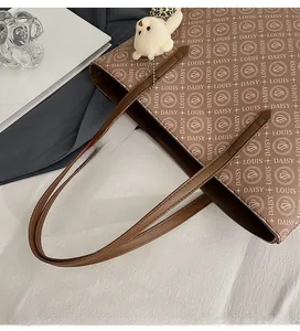 Brown tote bag detail with letter logo pattern and white plush bear ornament