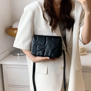 Puffy puzzle-quilted crossbody bag in black leather style worn by a model in white blazer