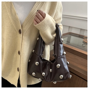 Détail d'un sac à main chocolat avec des rivets argentés et une anse plissée