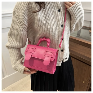 Detail of rose pink square bag with pleated handle and retro buckles on beige cardigan
