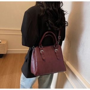 Détail d'un sac à main bordeaux en cuir ciré avec finitions argentées et bandoulière