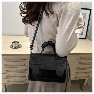 Detail of black faux leather bag featuring a ruched handle and dual buckle closure