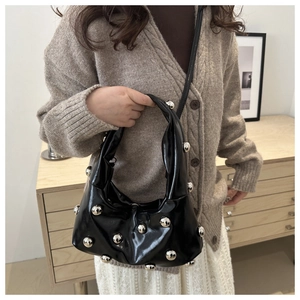 Détail du sac hobo en cuir verni noir avec gros clous argentés et design plissé
