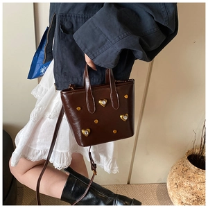 Detail shot of a brown patent leather tote bag with heart rhinestones and gold rivets