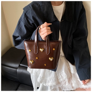 Detail of dark brown leather tote bag with gold heart charms and metal rivet accents