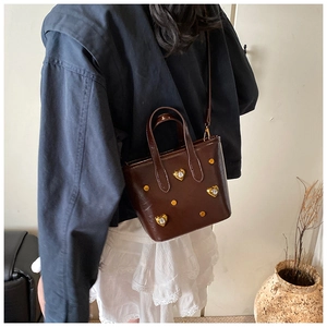 Detail of dark brown leather bucket bag with heart crystals and golden studs worn by model