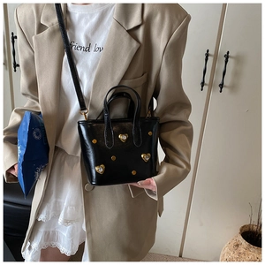 Detail of black mini tote bag with gold heart accents and rivets worn with a camel blazer