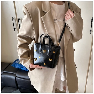Detail of a black leather bucket bag with gold heart rhinestones on a stylish model