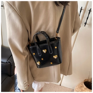 Detail of black rhinestone bucket bag with gold heart charms worn with a beige blazer