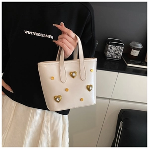 Detail of off-white bucket bag with golden heart-shaped crystal studs held by hand