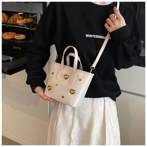 Detail of cream bucket bag with gold heart studs held in a cozy kitchen setting