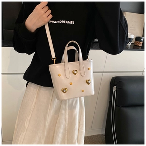 Detail of cream white bucket bag with gold heart rhinestones and studs on a model