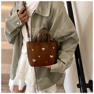Detail of a brown glossy leather bucket bag featuring heart rhinestones and gold studs