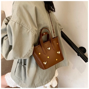 Brown leather bucket bag with gold heart studs worn by a model on a crossbody strap