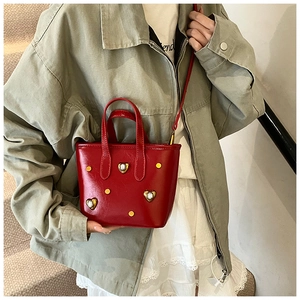 Detail of red bucket bag with gold heart clasp and crossbody strap shown on model