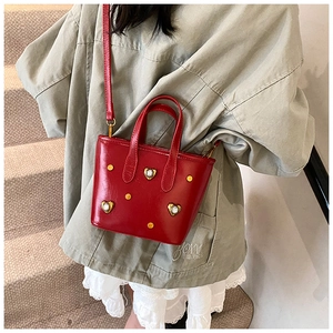 Detail of red patent leather bucket bag with gold heart-shaped rhinestone and stud accents