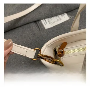 Detail view of the polished golden hardware hook and zipper on a white leather bucket bag