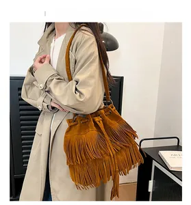 Brown suede tassel bucket bag shown on shoulder with long fringe and drawstring detail