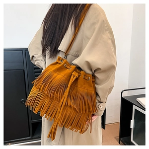 Detail of tan suede bucket bag with tiered fringes and drawstring closure on shoulder
