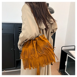 Detail of a ginger suede bucket bag with tiered fringes and drawstring closure on a model