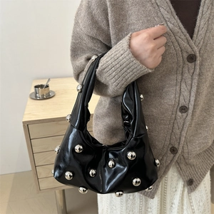 Sac à main noir brillant à rivets et boules argentées dans un intérieur de maison chic