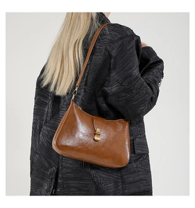 Brown vintage baguette bag with gold buckle on model wearing a textured black coat
