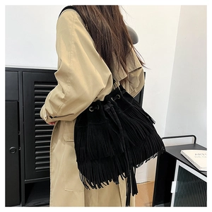 Detail view of black faux suede bucket bag with tiered tassels and drawstring on model