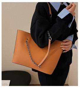 Chic orange leather tote bag with silver chain strap shown on model's shoulder