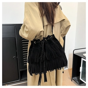 Detailed view of a black suede bucket bag with long tassels on a model in a beige coat