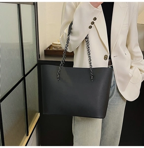Detail of minimalist black leather tote bag with thick metallic chain handles for women