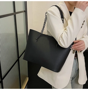 Detail of matte black tote bag with metal chain strap worn over a white suit jacket