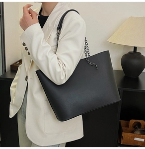 Detail of a large black tote bag featuring chain-link straps on a white suit model