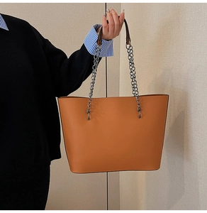 Detail of bright orange tote bag featuring a chunky silver chain handle and leather texture