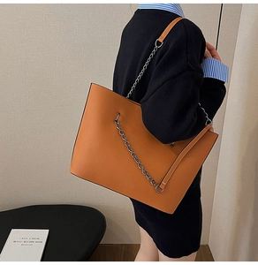 Detail of orange leather tote bag with thick gold chain strap on model shoulder