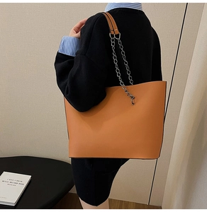 Detail of caramel brown tote bag featuring a metal chain strap on a model's shoulder