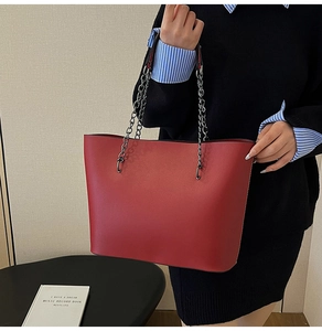 Detail of red leather tote bag with silver chain strap shown by a model for size comparison