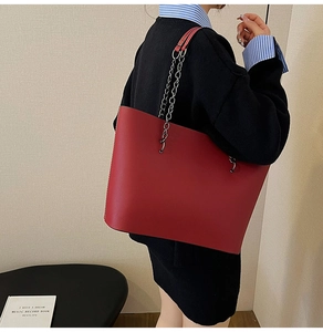 Close-up of red leather tote bag with silver chain strap worn by a female model
