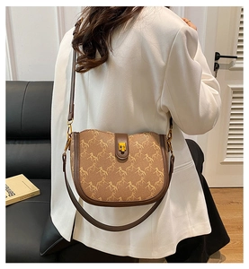 Detail shot of a brown saddle bag with vintage horse carriage print and gold metal buckle