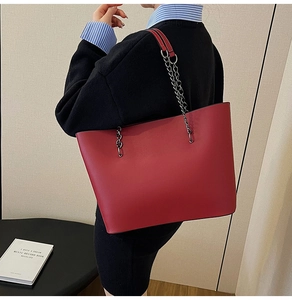 Detail of red leather tote bag with silver chain strap shown on a female model
