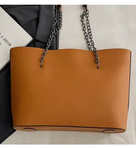 Close-up of tan leather tote bag with dark gunmetal chain straps on a textured surface