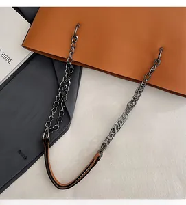 Close-up of tote bag silver chain strap and leather shoulder pad on textured background