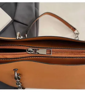 Close-up of smooth metal zipper and silver chain on vintage brown leather tote bag
