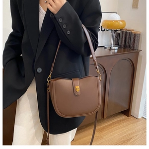 Detail of vintage brown leather saddle bag with gold T-shaped clasp on a fashion model