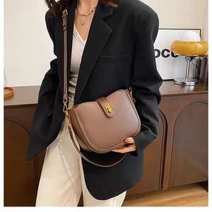 Detail of dark brown leather saddle bag featuring a vintage gold clasp and shoulder strap