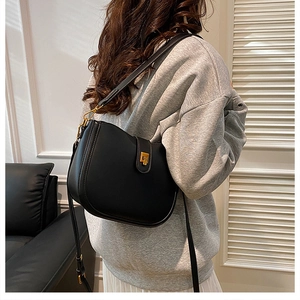 Detail of vintage black saddle bag showing matte leather texture and gold buckle on a model