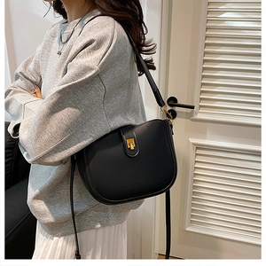 Classic black saddle bag worn cross-body over a grey sweatshirt and white pleated skirt